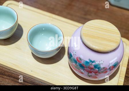 This image showcases a traditional floral teapot with a lid and two small ceramic cups on a light wooden tray, creating a cozy and decorative tea sett Stock Photo