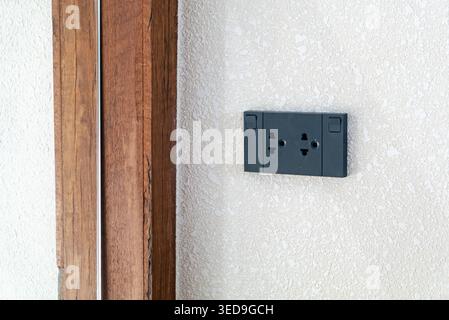 A sleek, modern wall socket installed on a white textured wall adjacent to a wooden panel, designed for easy access to electrical power in residential Stock Photo