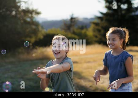 Two sisters blowing soap bubbles together in nature during spring day. Stock Photo
