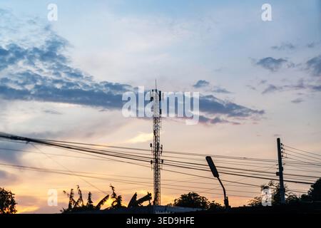 Scene showcasing a communication tower and power lines against a colorful sunset sky, emphasizing urban infrastructure and technology network with sil Stock Photo