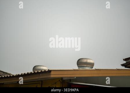 A view of metal turbine ventilation systems on an industrial rooftop, showcasing modern design and efficient air circulation against a gray sky backdr Stock Photo