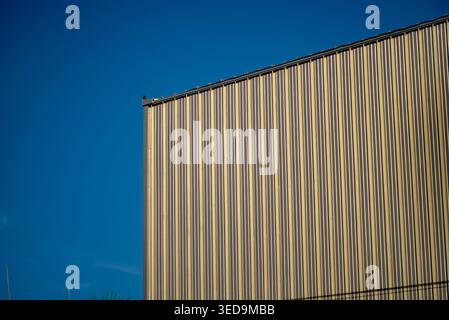 A close-up view of a striped metallic wall against a clear blue sky, highlighting modern architectural design and texture in an urban environment. Stock Photo