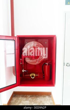 This image features a red fire equipment cabinet showcasing a hose reel and fire extinguisher, emphasizing safety measures in emergency situations. Stock Photo