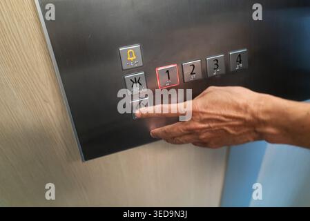 A close-up of a hand pressing an elevator button in a modern building. The image highlights the sleek design and functionality of elevator technology Stock Photo