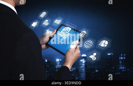 A business professional engages with a tablet displaying digital icons on a dark backdrop, symbolizing technology and finance in modern commerce and Stock Photo