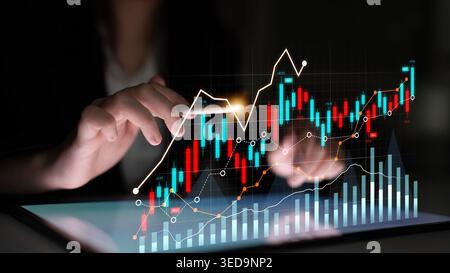 A business professional analyzes digital financial data on a tablet, featuring vibrant graphs and charts displaying upward trends in a modern and dark Stock Photo