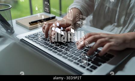 A person typing on a laptop keyboard, surrounded by floating digital icons representing technology and connection, showcasing modern workspace Stock Photo