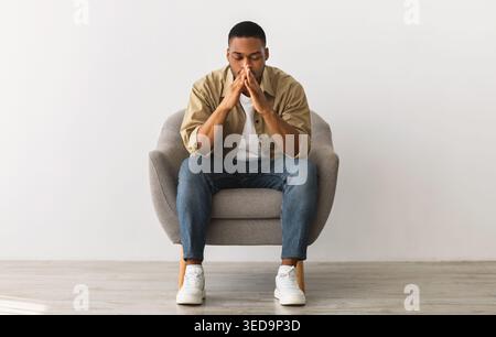 Frustrated African Guy Thinking About Problems Sitting Over Gray Wall Stock Photo