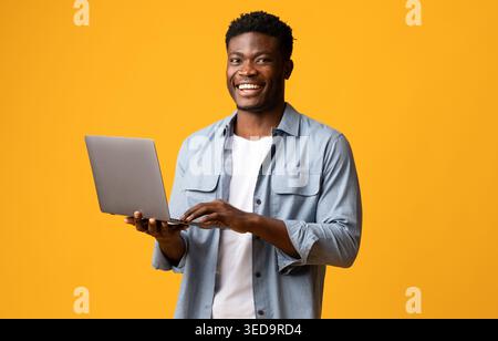 Handsome black man using modern laptop on yellow Stock Photo