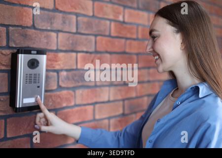 Woman pressing button on intercom panel near brick wall Stock Photo