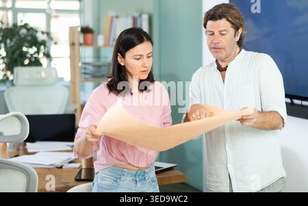 Middle-aged man and woman discussing construction plan standing in office Stock Photo