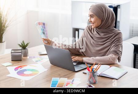 Muslim woman designer working with color palette and laptop in office Stock Photo