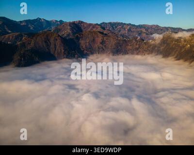 Aerial view of thick white clouds filling a valley surrounded by rugged mountain peaks under a clear blue sky Muzaffarabad, Azad Kashmir, Pakistan. Stock Photo