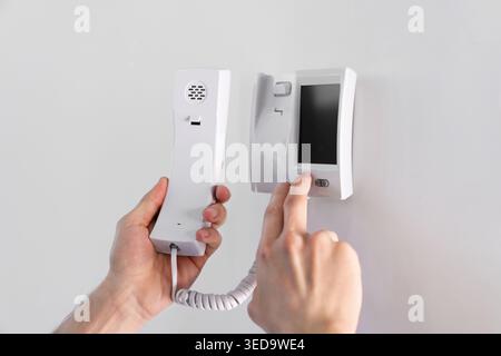 Man with handset pressing button on intercom panel indoors, closeup Stock Photo