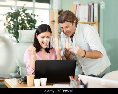 Happy colleagues sharing success while looking at laptop screen Stock Photo
