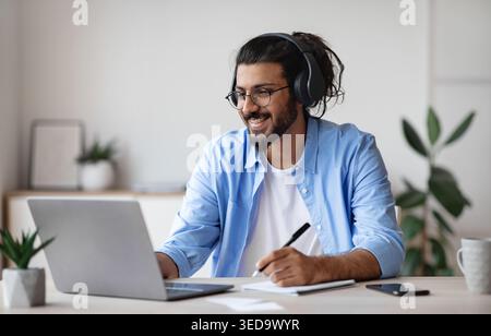 Distance Learning. Indian Guy Watching Webinar On Laptop Computer And Taking Notes Stock Photo