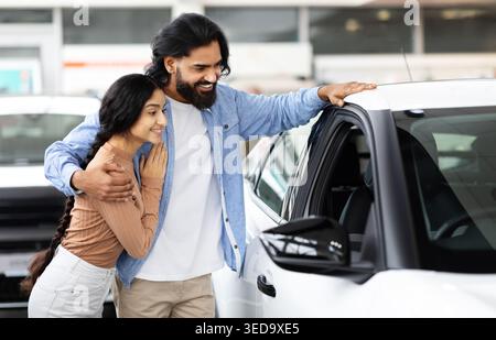 Smiling eastern couple looking inside beautiful white auto in showroom Stock Photo