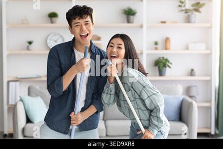 Positive chinese lovers having fun while cleaning house Stock Photo