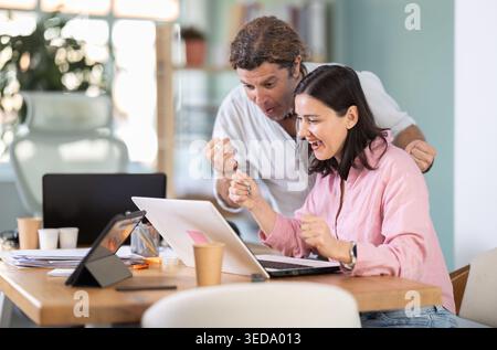 Happy colleagues sharing success while looking at laptop screen Stock Photo