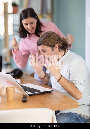 Happy colleagues sharing success while looking at laptop screen Stock Photo