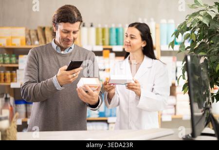 Middle-aged man scanning QR-code on pills box while pharmacist offering Stock Photo