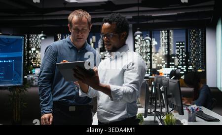 Teamworking tech startup coworkers using tablet, brainstorming ways to optimize performance in office. Technicians use machine learning on digital device for debugging, analyzing code Stock Photo