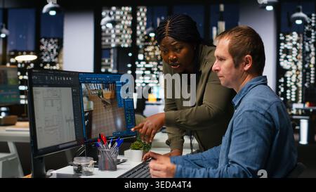 Diverse engineers team creates 3D render of apartment interior with architectural software and blueprints. Using computer with modern tools and models to allow customization of flooring. Camera B. Stock Photo