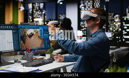Male engineer using VR headset and AI on interior design software at workstation, moving assets for apartment layout with artificial intelligence suggestions in 3D render program. Camera B. Stock Photo