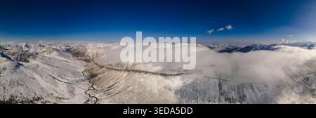 Aerial view of Babusar Pass winding through snow-capped mountain peaks under a clear blue sky with rolling clouds in Babusar, KPK, Pakistan. Stock Photo