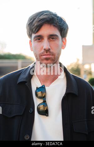 Thoughtful young adult man with sunglasses resting on his collar is gazing confidently with a serious expression, showcasing a moment of reflection Stock Photo
