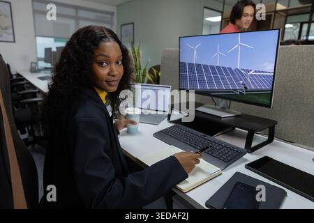 External monitor is showing solar panels and wind turbines while laptop is running at office desk Stock Photo