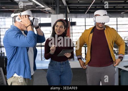 Coworkers with senior man testing white VR headsets while woman holding tablet in open-plan office Stock Photo
