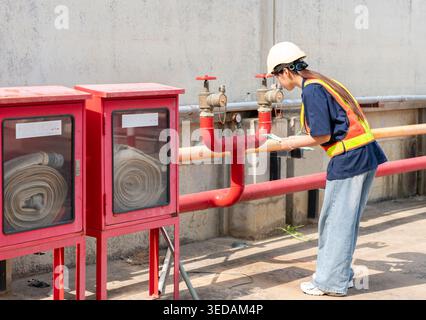 Professional inspector conducting a routine safety audit and maintenance check of fire protection systems at an outdoor factory site. Stock Photo