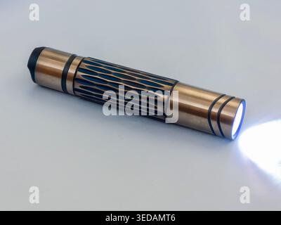 Titanium handheld flashlight on sky blue background Stock Photo