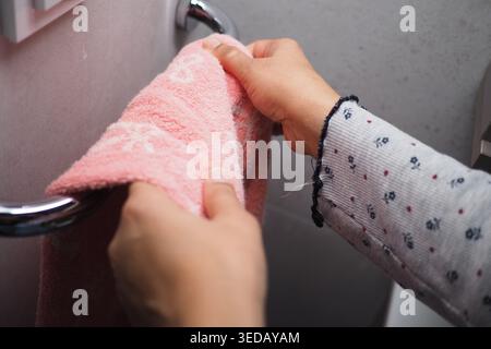 Hands hold a pink towel while reaching for the towel rack Stock Photo