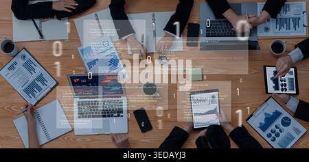 A business team collaborates in a modern workspace, analyzing data on laptops and tablets with documents spread out, reflecting productivity and Stock Photo