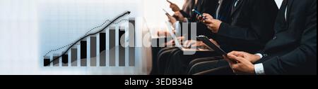 Group of business professionals engaged with devices, analyzing important financial data and collaborating during a presentation in a modern corporate Stock Photo