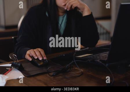 Stressed woman working on laptop with hand on chin. Serious female person using computer mouse, thinking about problem or cyberbullying concept. Stock Photo