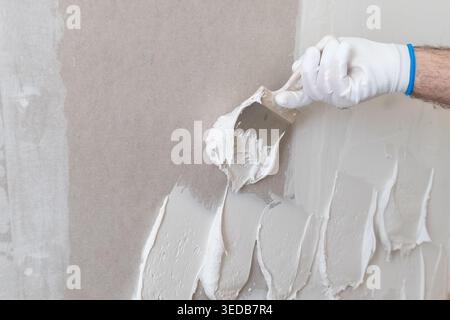 A skilled worker spreads a layer of plaster using a trowel on an interior wall surface. The workspace is well lit, showcasing the texture of the material and the precision in application. Stock Photo