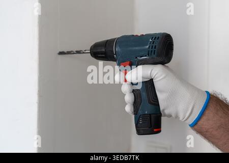 Using a cordless drill to create holes in wall during installation process. Gloved hand grips the tool firmly, with focus on precision and safety while working. Stock Photo