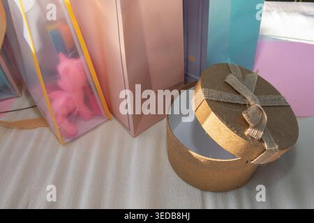 Round gift box with ribbon and colorful shopping bags on table festive present packaging concept Stock Photo