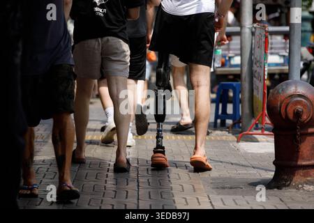 BANGKOK, THAILAND-MAR 29, 2026: Disabled man with prosthetic leg walking with friends, travel exploration through city walking, high angle view Stock Photo