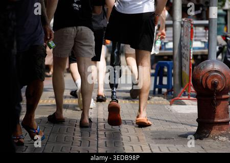 BANGKOK, THAILAND-MAR 29, 2026: Disabled man with prosthetic leg walking with friends, travel journey unfolding step by step, high angle view Stock Photo
