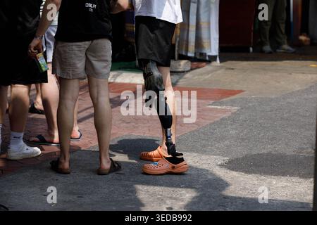 BANGKOK, THAILAND-MAR 29, 2026: Disabled man with prosthetic leg walking with friends, travelers discovering a new destination, high angle view Stock Photo