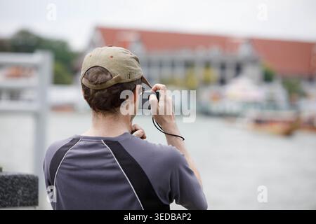 Male tourist using digital camera to take travel photo, travel lifestyle and digital behavior, rear view. Stock Photo