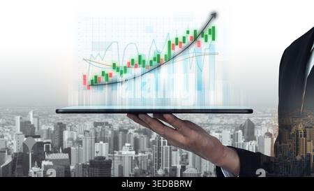 A businessman holds a laptop displaying a vibrant financial growth chart over a sprawling cityscape, representing modern investment success and Stock Photo