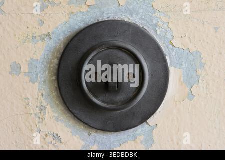 Old round Bakelite light switch on a wall with weathered paint Stock Photo