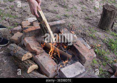 Close view of person preparing outdoor campfire with branches and wooden logs in handmade brick fire pit at countryside backyard cottage Stock Photo
