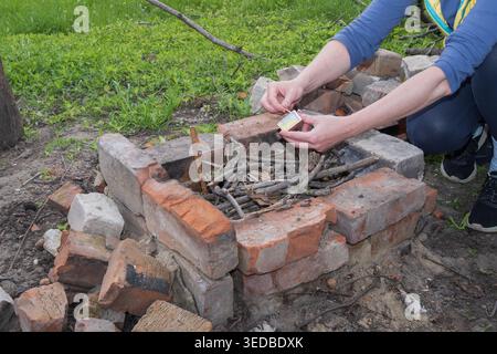 Rustic brick fire pit with person preparing branches for outdoor campfire in backyard area Stock Photo