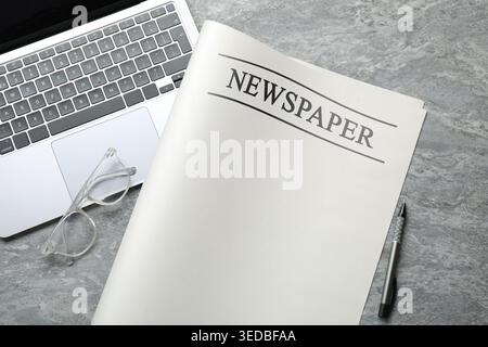Newspaper, laptop, glasses and pen on grey desk, flat lay Stock Photo
